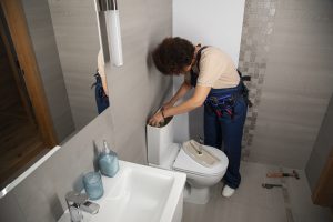 woman repairing a toilet with the tank lid removed